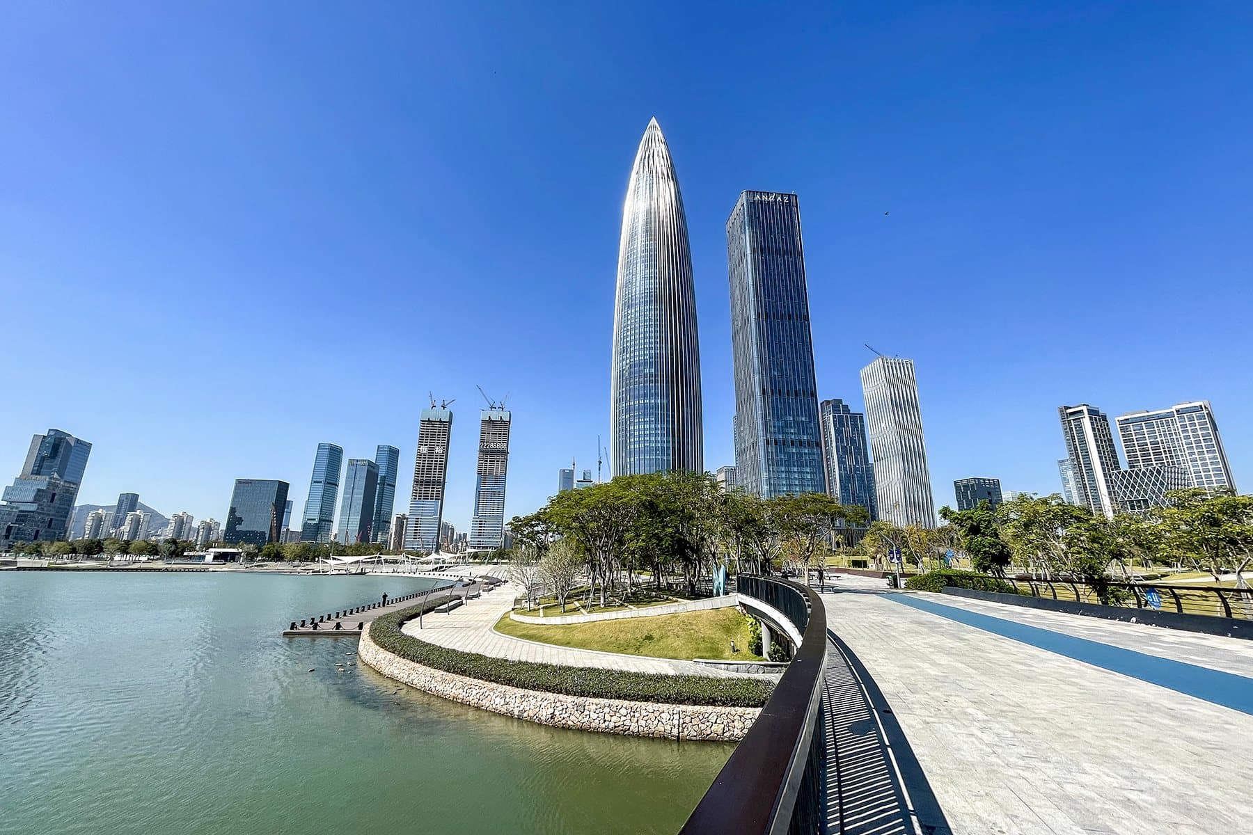 Skyscrapers along Shenzhen Bay rise above a curving waterfront promenade and still water under a deep blue sky