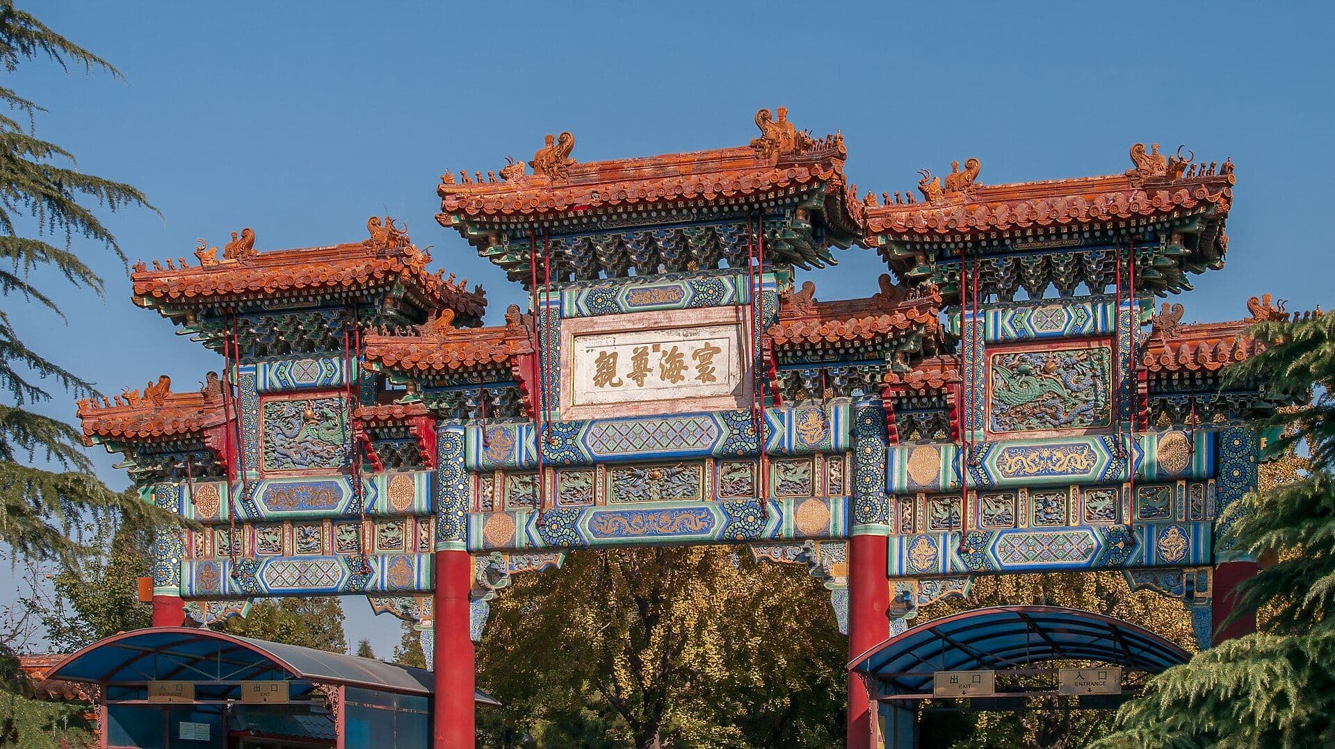 An ornate memorial archway at Beijing's Lama Temple, with orange-tiled roofs and blue, green and gold painted beams against a clear sky