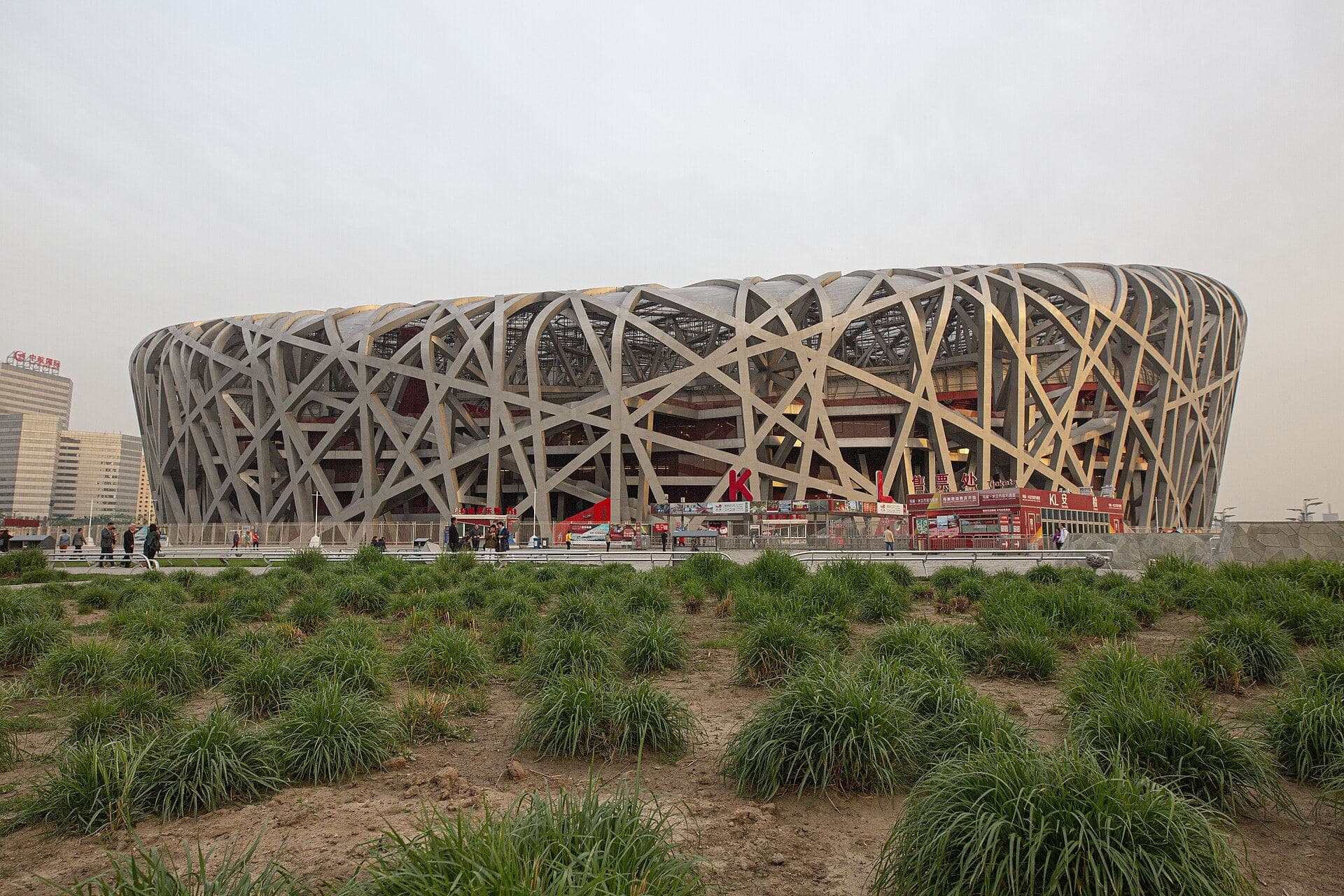 The steel lattice of the Beijing National Stadium (Bird's Nest) above a grassy foreground under a pale sky