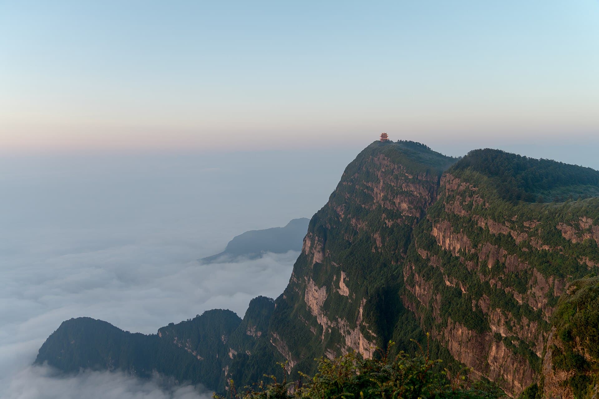 Mount Emei's sheer cliff summit rising above a sea of clouds at dawn, a temple on top