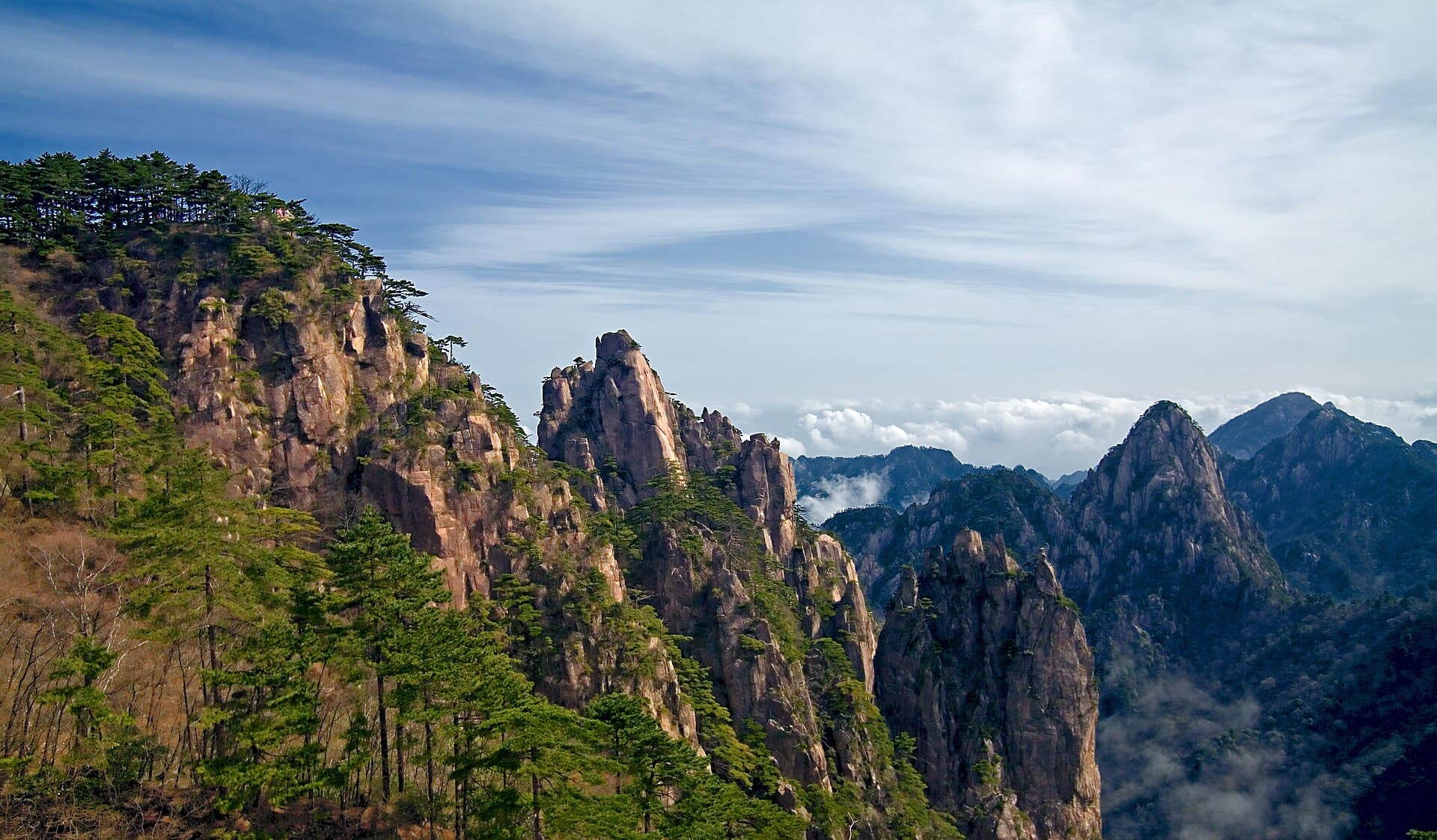 Granite peaks and pine-covered cliffs of Huangshan, with drifting cloud and a blue sky