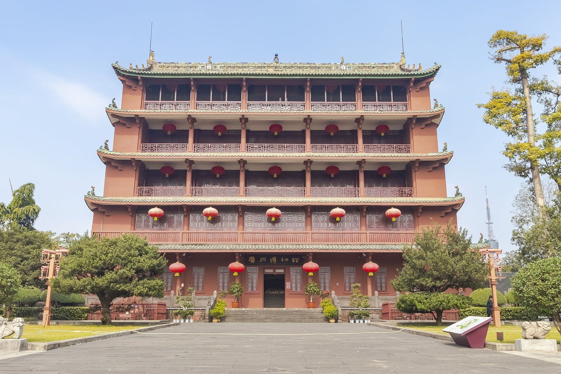 The five-storey red Zhenhai Tower in Yuexiu Park, Guangzhou, hung with red lanterns and framed by pine trees under a blue sky