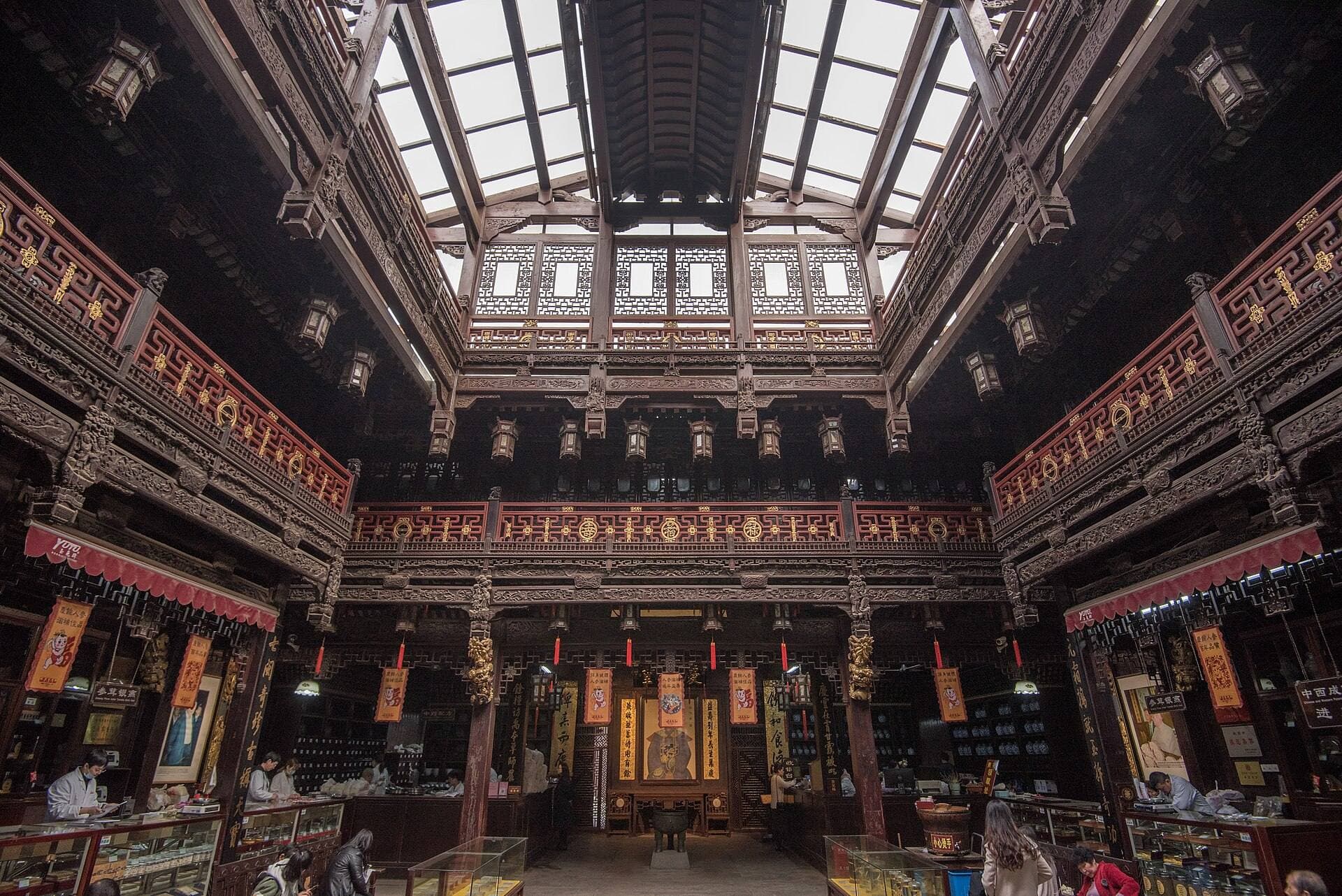 The skylit atrium of the historic Hu Qing Yu Tang pharmacy in Hangzhou, with carved dark-wood galleries, lanterns and medicine counters
